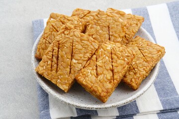 Tempeh, Tempe Goreng or Fried tempeh is Indonesia traditional food, made from fermented soybean seeds wrapped in banana leaves. Salty and savory, served as a side dish or snack. Served on plate.
