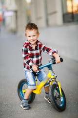 Fototapeta na wymiar Stylish boy ride on balance bike on sidewalk in city