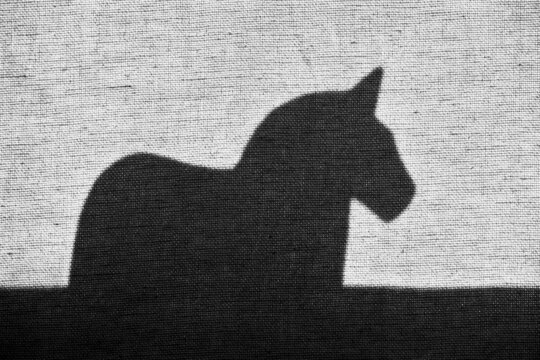 shadow of black and white wooden horse standing in a window sill behind a curtain