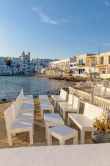 Traditional Cycladitic view with an exterior of a bar besides the sea and  whitewashed houses with the christian church of kimisis Theotokou during afternoon in Naousa  Paros island, Greece