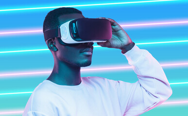 Serious African male in white sweatshirt using hi tech smart vr glassses over neon background