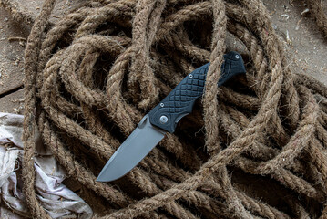a folding knife lying on a thick rope. on the background of a wooden floor