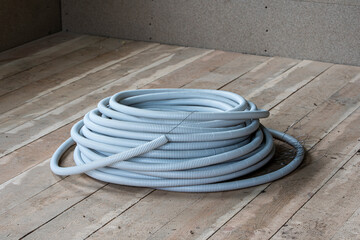 a large coil of plastic corrugation for electrical cables lies on the floor in a frame house under...