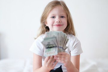 Smiling beautiful little girl is holding fan of dollars.