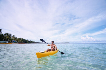 Young strong man kayaking in the sea near the tropical island. Adventure by kayak.