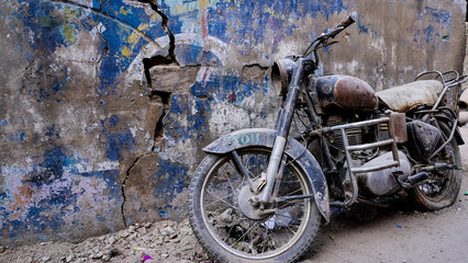 Old black Indian Royal Enfield motorcycle against a very colorful blue wall in India, wide shot