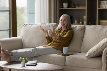 Happy excited mature 50s smartphone user woman speaking on video conference call, talking to family online, smiling, laughing, sitting, relaxing on couch at home, taking selfie,