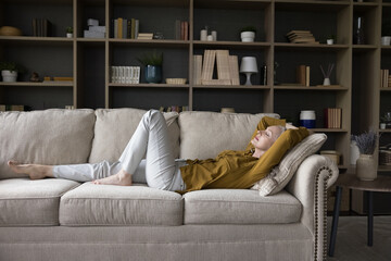 Peaceful calm mature woman lying on sofa with closed eyes, sleeping, stretching body, enjoying...