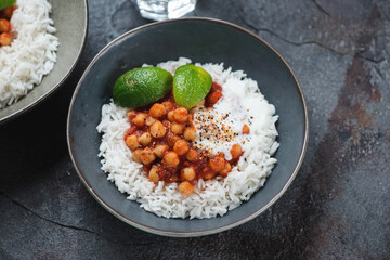 Bowl of indian chana masala or chickpeas in a spicy onion tomato masala with basmati rice, middle close-up on a dark-grey stone background, studio shot