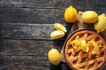 Delicious lemon tart,  pie with cooking ingredients on the wooden table, fresh lemons fruits around	