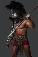 Shot of ancient roman fighter with plumed helmet throwing spear against grey background.