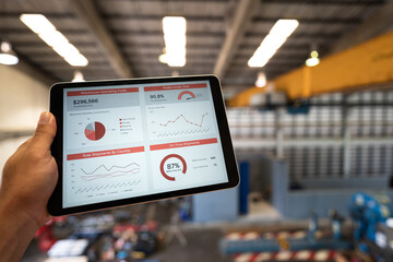 Action of manager is looking at logistic summary information on tablet with factory warehouse as...