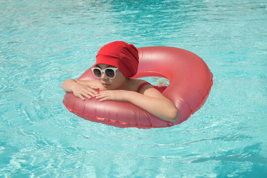young woman in vintage red bathing suit and inflatable ring in swimming pool in summer sun