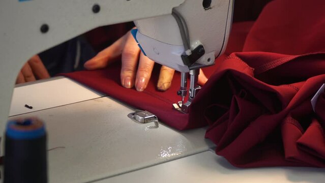 Woman's hands sew on a sewing machine. A girl with a beautiful manicure puts a straight stitch on a light knitted fabric.