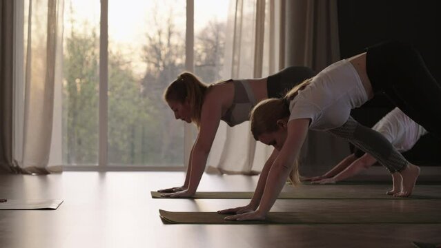 In slow motion, a joint female Pilates workout with an instructor shows thin and plump women in the gym in the morning in the sun. The glare of the sun on the floor