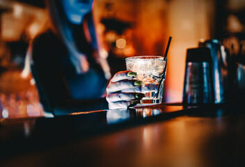 Woman bartender holding cold gin tonic cocktail in bar