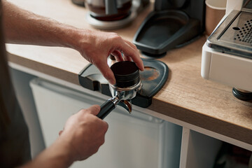 Photo of barista hands holding portafilter and coffee tamper preparing coffee tablet