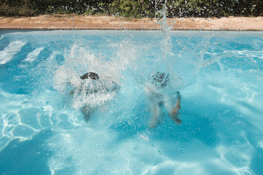 girl and boy jumping in the swimming the pool in summer with splash