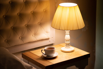 Lampe sur la table de chevet. Lampe de chevet à lumière chaude. Lire un livre au lit sous une lampe. Thé au lit le soir. Chaude soirée. Automne
