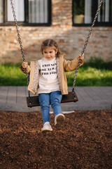 Happy little girl swing on a swing in the specially designated place in the park. Softner from...