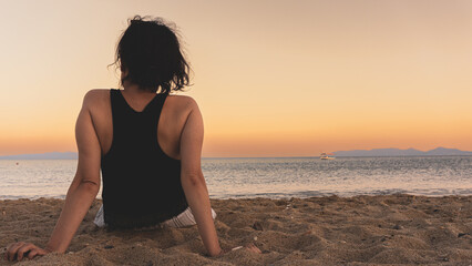 Alone single woman sitting on sand at sunset, looking at distant sea or seascape horizon. Missing...