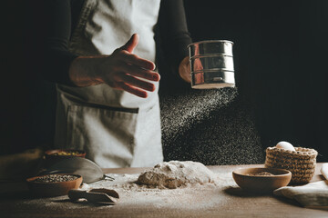 Young man kneading dough on dark background.
