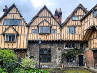 Fototapeta na wymiar Cheney Court and old medieval stables view in Winchester. Half timbered tudor architecture. Yellow half timbered tudor house near Cathedral in Winchester. Stables. Through the gate.
