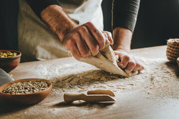 Young man kneading dough on dark background. - obrazy, fototapety, plakaty