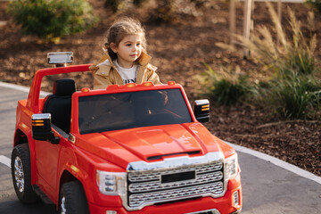 Cute little girl rides in a mini city on a red electric car jeep. Adorable little girl road in toy...