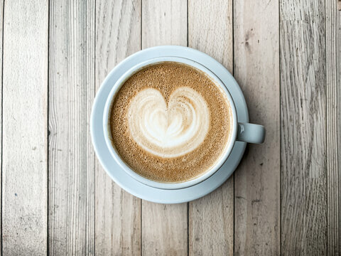 A cup of coffee latte On a wooden table. A mug of flat white coffee on a wooden background. Coffee art. Heart flower shape latte art. Copy space