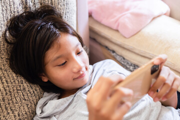 Obraz na płótnie Canvas Asian youth kid lying down using smartphone browsing internet content, social media