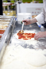 chef extendiendo tomate en la masa de un pizza