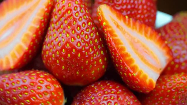 Strawberries close-up, macro. Berries rotate on their axis. Concept of delicious dessert, horticultural harvest. Halves and lobes of jacogds lie beautifully along with whole berries. No tails.