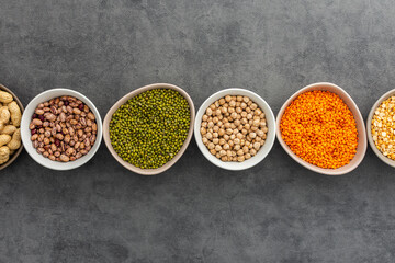 Different types of legumes in bowls, yellow peas and chickpeas , beans and peanuts, maash and lentils, top view, copy space