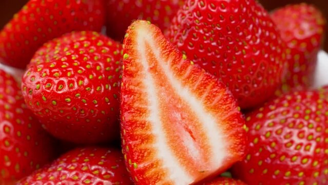 Strawberries close-up, macro. Berries rotate on their axis. Concept of delicious dessert, horticultural harvest. Halves and lobes of jacogds lie beautifully along with whole berries. No tails.