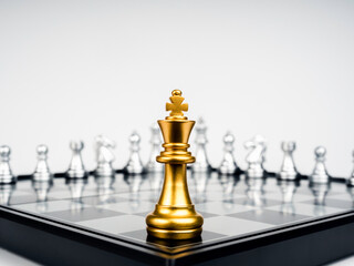 The Golden king chess piece standing on chessboard corner in front of many silver chess pieces on...