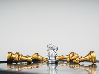 The gold horse, knight chess piece standing with falling silver pawn chess pieces on chessboard on...