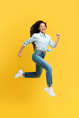 Fototapeta na wymiar Excited young woman jumping up at orange studio