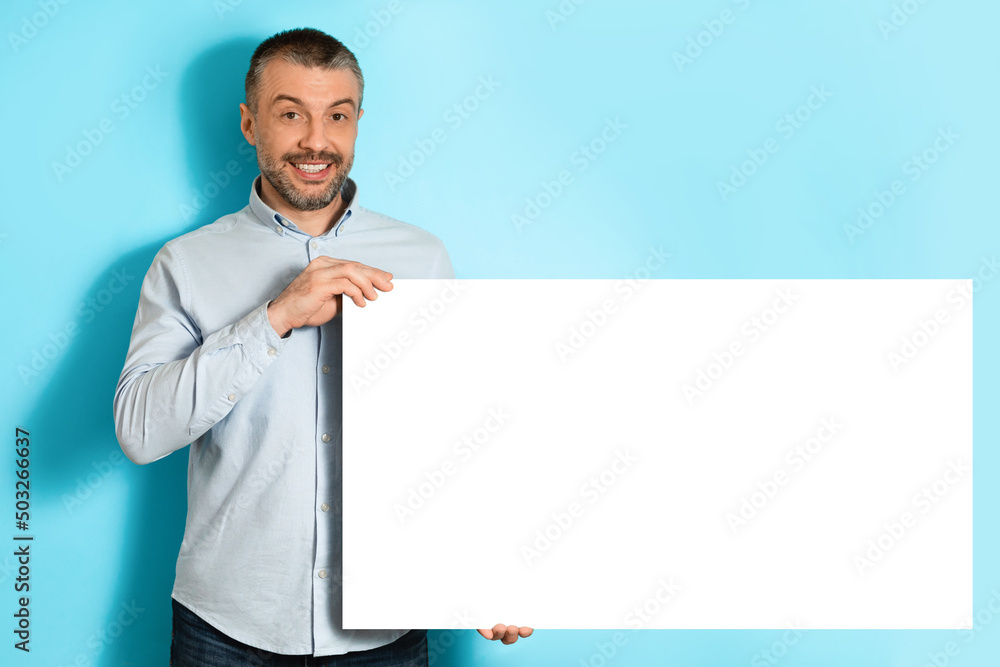 Poster middle aged man showing empty paper board over blue background