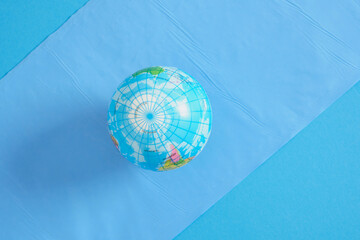 Globe ball and blue trash bags on blue background. Creative concept with planet Earth in plastic trash bag.
