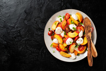 Summer peach Caprese salad with mozzarella and cherry tomatoes. Black background, top view