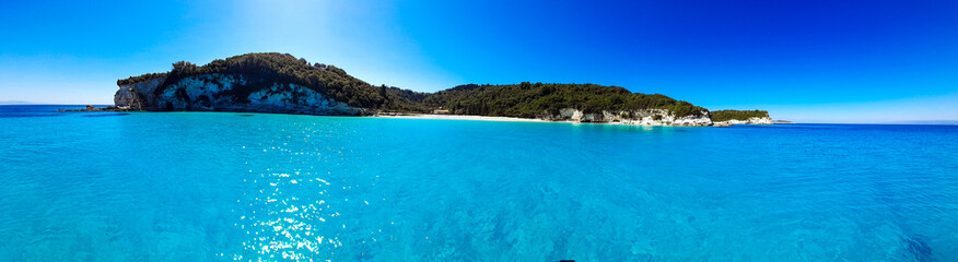 Panoramic view of deserted island with trees and sand beach set on azure blue crystal clear ocean sea water. With copy space.