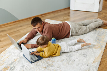 Dad and son are lying on the floor with computers. Dad teaches his son programming. Children's computer.