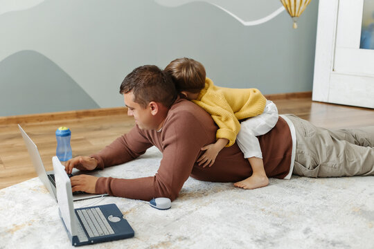 Dad and son are lying on the floor with computers. Dad teaches his son programming. Children's computer. - Powered by Adobe