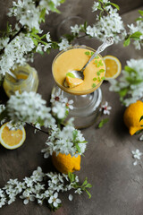 Lemon cream in a beautiful glass goblet on a table among lemons and flowering branches.