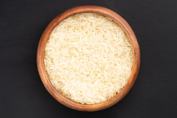 Long Basmati rice in wooden bowl on black wooden background. Macro. Flat lay. Vegetarian food concept