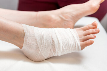 Female foot is bandaged. Ankle injury. Beautician leg wrap. Cosmetic procedure. Close up.