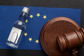 Alcohol lawsuit in European Union concept. Wooden judge gavel and bottle of alcohol on EU flag...