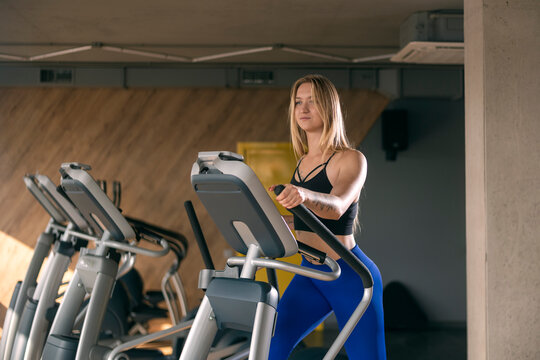 Beautiful sexy young woman with blonde hair is engaged on an orbitrek elliptical trainer. Cardio workout in the gym.