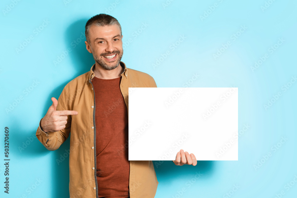 Poster smiling man showing blank paper poster standing over blue background